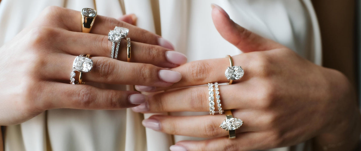 Woman photography with multiple diamond engagement rings and wedding bands stacked on both hands.
