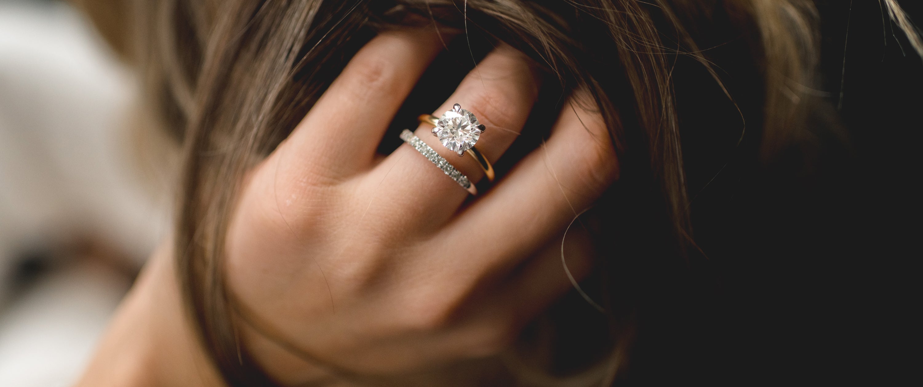 Woman with hand on her hair and close up on diamond round engagement ring and pave wedding band